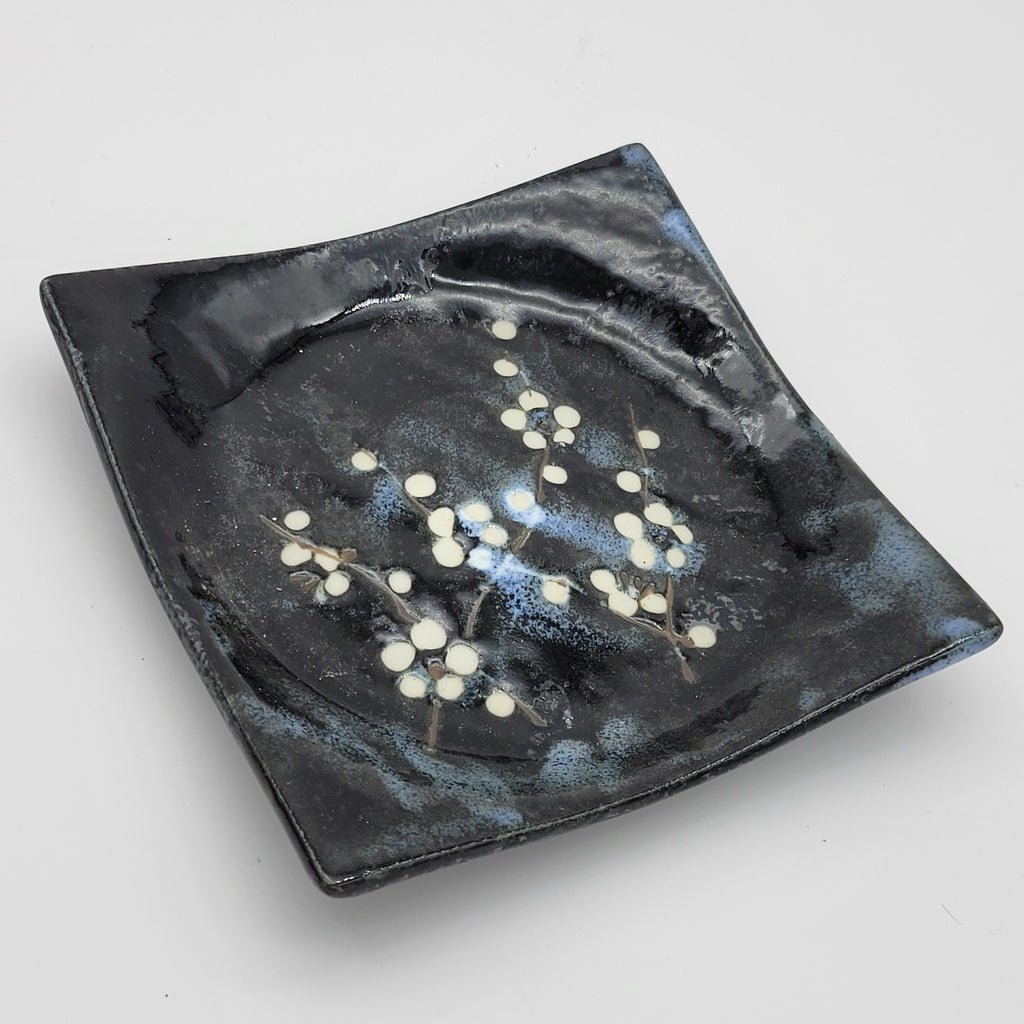 Close-up of black square ceramic plate with white blossom design