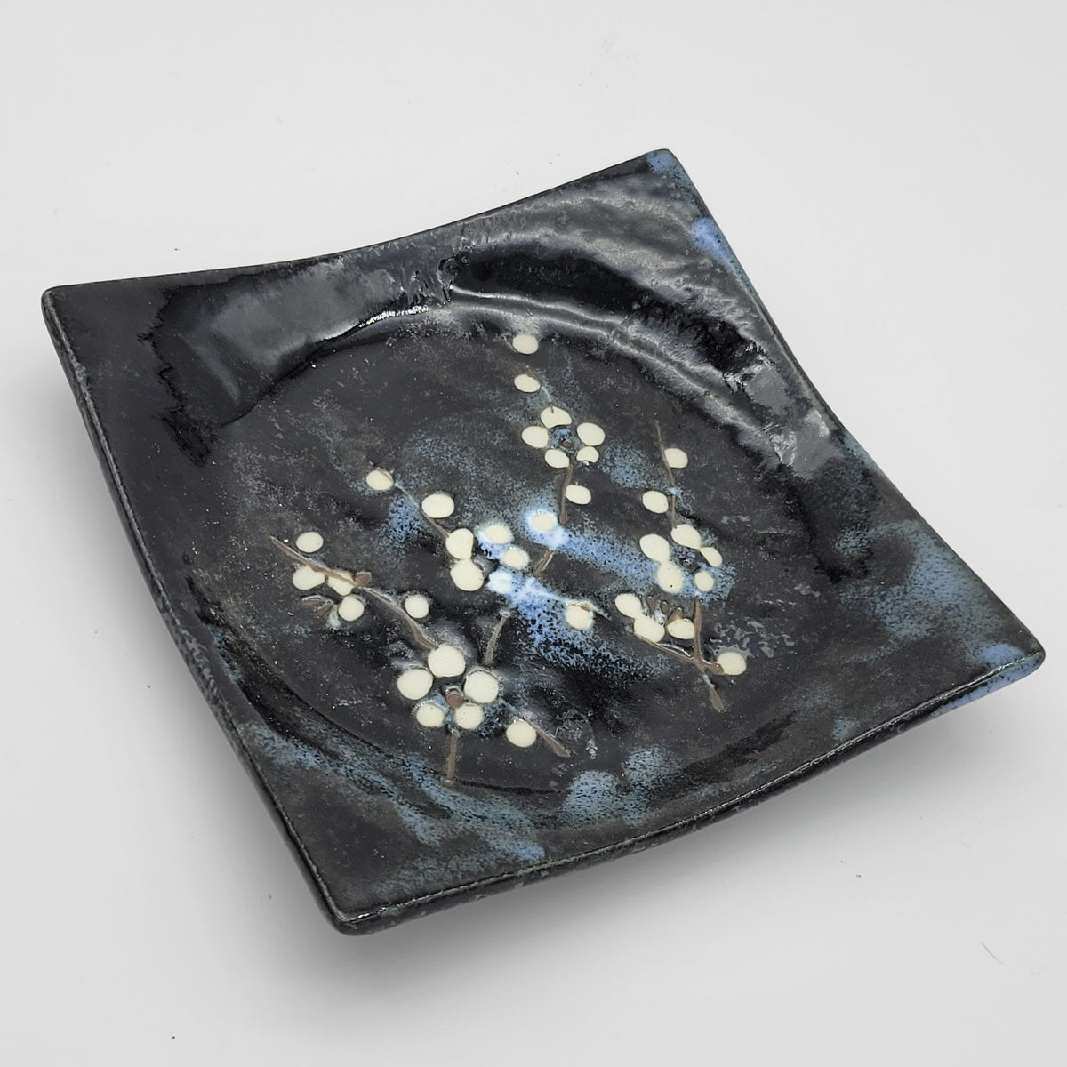 Close-up of black square ceramic plate with white blossom design